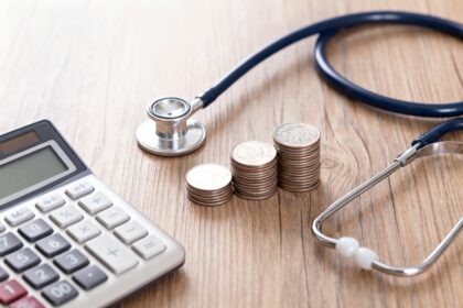Calculatrice, pièces de monnaie et stéthoscope posés sur un bureau en bois