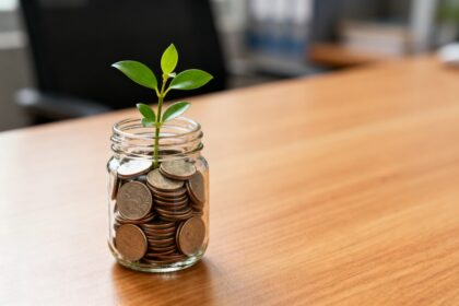 Bocal en verre rempli de pièces avec une petite plante verte qui pousse, posé sur un bureau